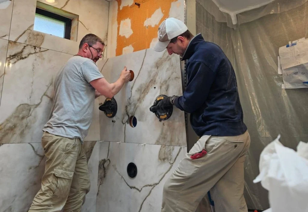 Two Bathroom Remodelers Installing Tile In Modern Bathroom